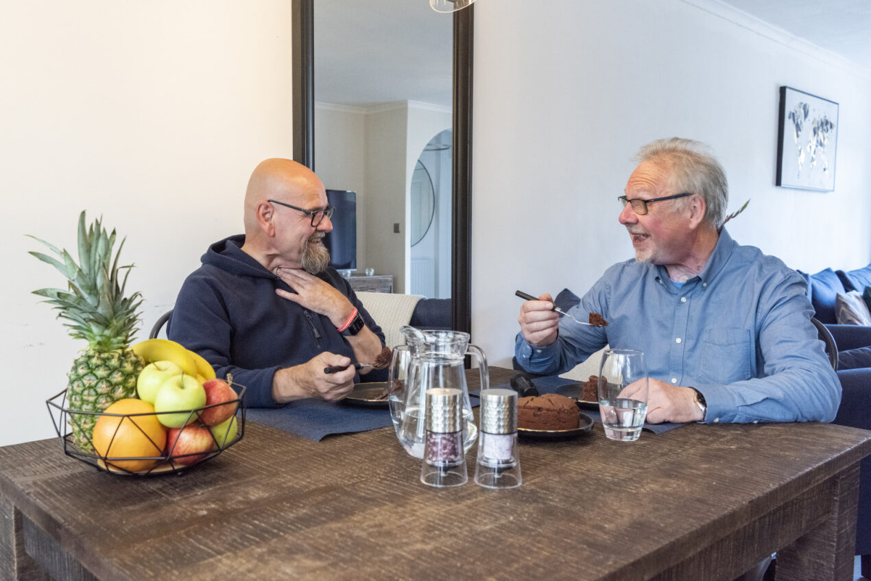 man with neck stoma using provox life hme talking to man at dining table